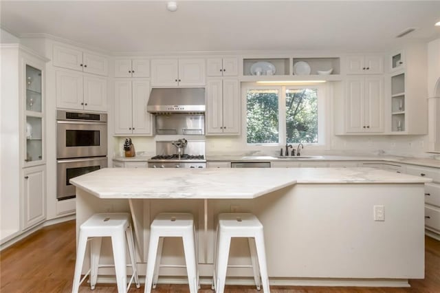 kitchen featuring white cabinets, hardwood / wood-style floors, stainless steel appliances, wall chimney exhaust hood, and a kitchen island