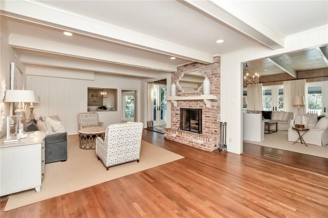 living room featuring beamed ceiling, hardwood / wood-style floors, wooden walls, a chandelier, and a brick fireplace