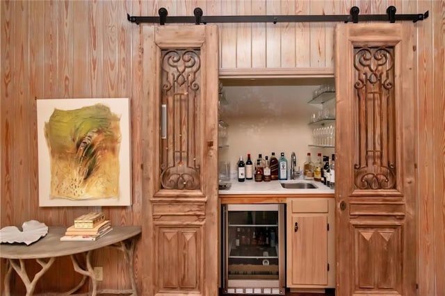 bar featuring a barn door, wooden walls, wine cooler, and sink