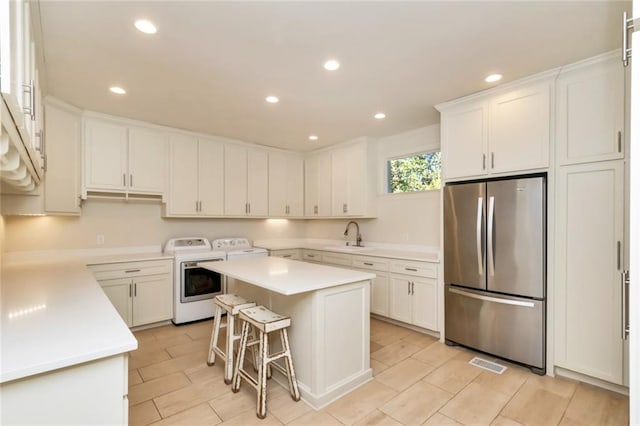 kitchen featuring a kitchen island, white cabinetry, washing machine and clothes dryer, and stainless steel refrigerator