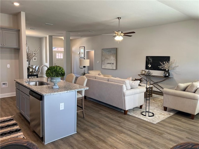 kitchen featuring dishwasher, sink, light stone counters, gray cabinets, and a center island with sink