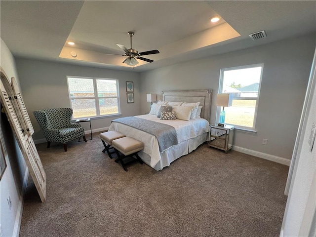 bedroom featuring ceiling fan, dark colored carpet, and a tray ceiling