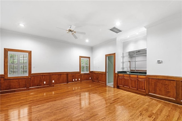 unfurnished living room with ceiling fan, light hardwood / wood-style floors, a healthy amount of sunlight, and ornamental molding