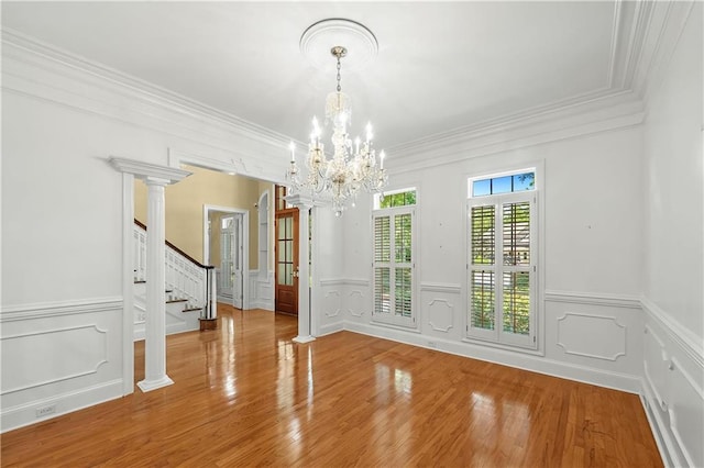 unfurnished dining area with decorative columns, hardwood / wood-style floors, a chandelier, and ornamental molding