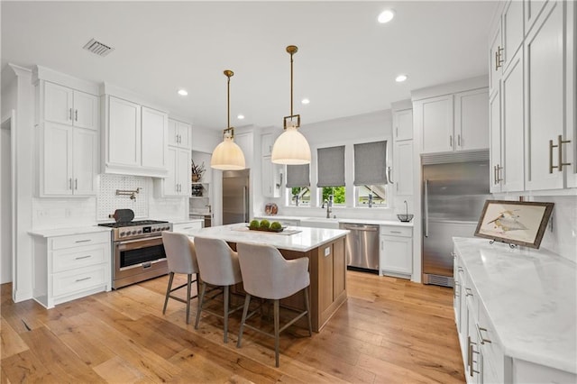 kitchen with premium appliances, a kitchen breakfast bar, decorative backsplash, a center island, and white cabinets