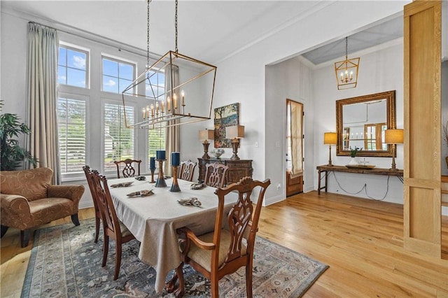 dining space with a chandelier, wood finished floors, crown molding, a high ceiling, and baseboards