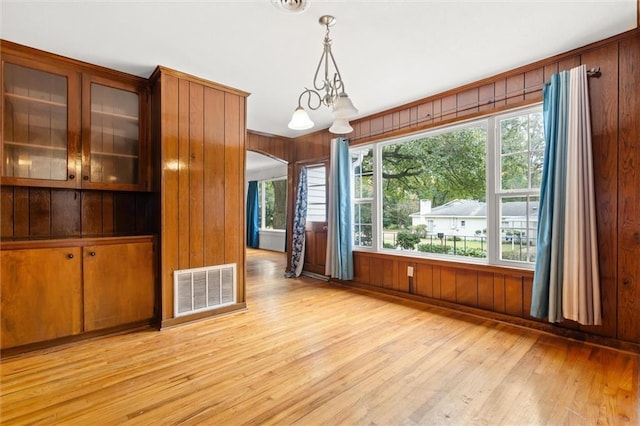 unfurnished dining area featuring a wealth of natural light, wooden walls, light hardwood / wood-style flooring, and an inviting chandelier