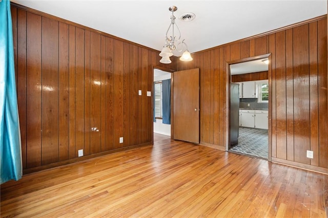 unfurnished room featuring a notable chandelier, wooden walls, and light hardwood / wood-style floors