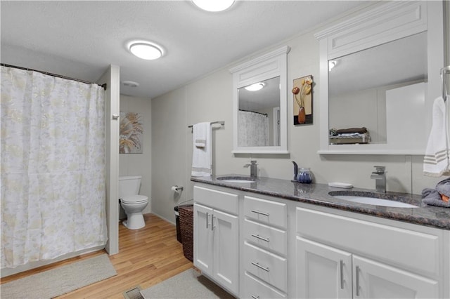 bathroom featuring double vanity, a sink, wood finished floors, and toilet
