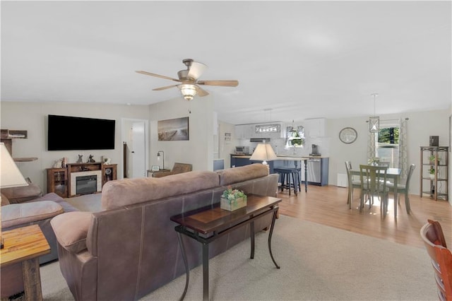 living room featuring light wood-style floors, a ceiling fan, and a glass covered fireplace