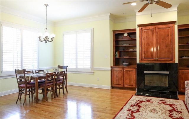 dining room with crown molding, a tile fireplace, light hardwood / wood-style flooring, and a wealth of natural light