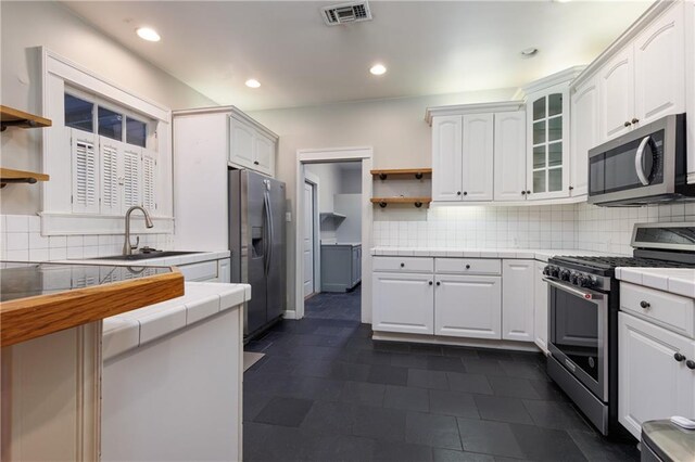 1660 Laurel St, Mobile, AL 36604 - kitchen with appliances with stainless steel finishes, open shelves, tile countertops, white cabinetry, and tasteful backsplash