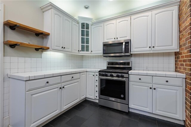 1660 Laurel St, Mobile, AL 36604 - kitchen with stainless steel appliances, tile counters, brick wall, decorative backsplash, and white cabinets