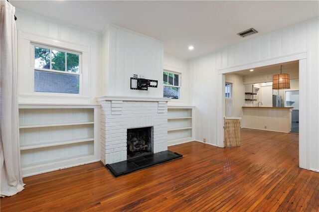 1660 Laurel St, Mobile, AL 36604 - unfurnished living room with wood-type flooring, a fireplace, a decorative wall, recessed lighting, and built in shelves