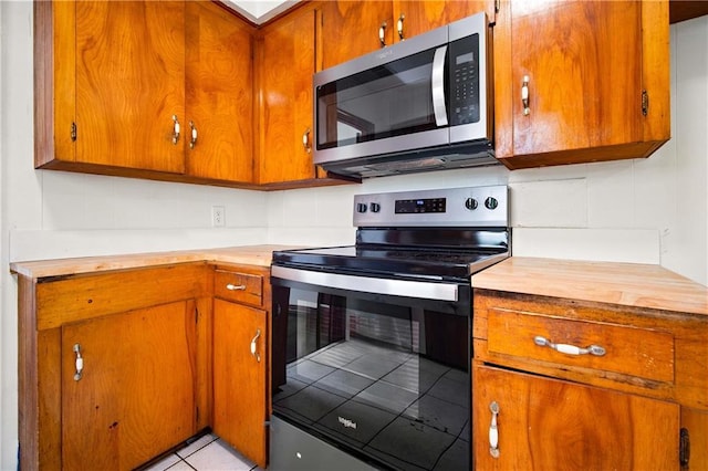 754 Pinemont Dr, Mobile, AL 36609 - kitchen with stainless steel microwave, range with electric stovetop, brown cabinetry, and light tile patterned floors