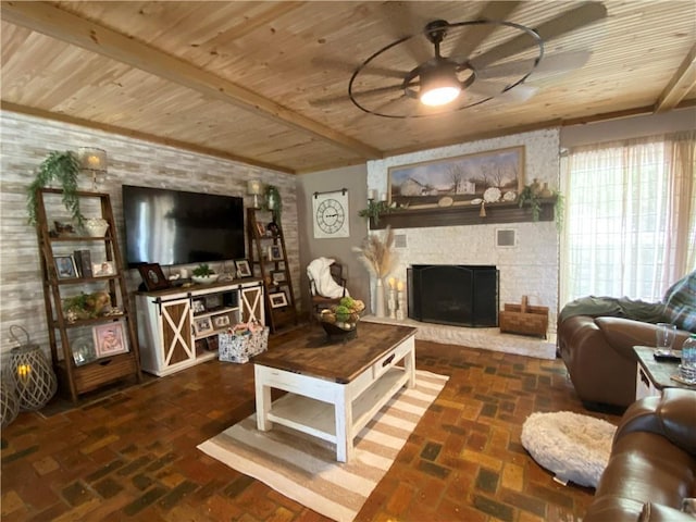 living area with ceiling fan, a stone fireplace, wood ceiling, and brick floor