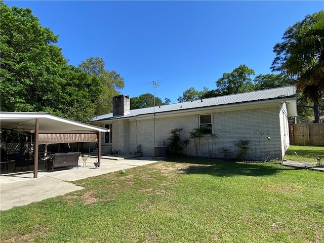 view of side of home with a chimney, a patio area, brick siding, fence, and a yard