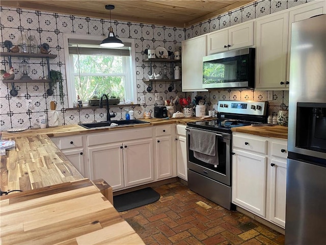 kitchen featuring open shelves, wallpapered walls, a sink, wood counters, and stainless steel appliances