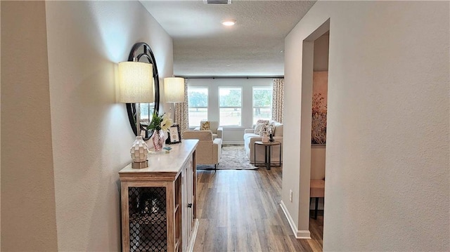 hallway with baseboards, a textured wall, wood finished floors, and visible vents