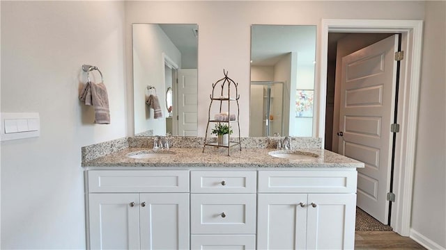 bathroom with baseboards, a sink, a shower stall, and double vanity