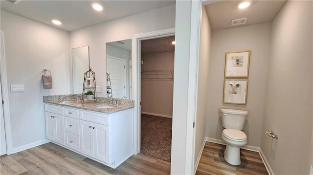 bathroom with a sink, double vanity, toilet, a spacious closet, and wood finished floors