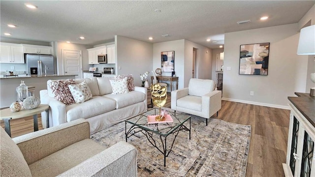living area featuring a textured ceiling, visible vents, baseboards, recessed lighting, and wood finished floors
