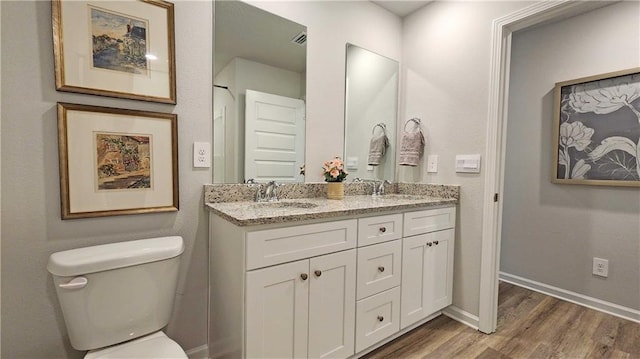bathroom with double vanity, wood finished floors, toilet, and a sink