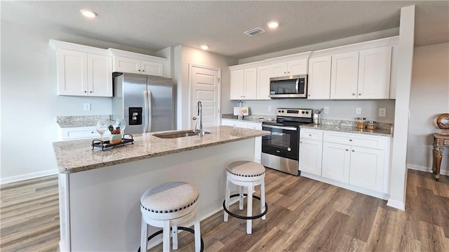 kitchen featuring wood finished floors, a sink, a center island with sink, appliances with stainless steel finishes, and visible vents