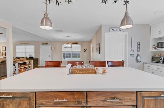 kitchen featuring stainless steel microwave, a center island, decorative light fixtures, light countertops, and white cabinets