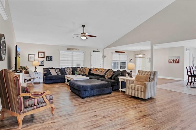 living room with baseboards, high vaulted ceiling, light wood-style flooring, and ceiling fan with notable chandelier