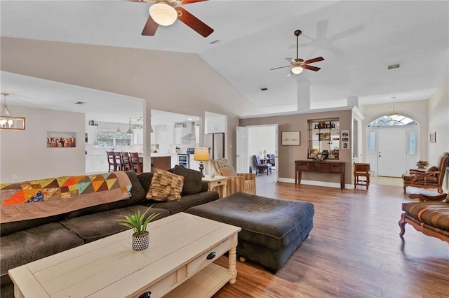 living room with visible vents, lofted ceiling, ceiling fan with notable chandelier, light wood finished floors, and baseboards