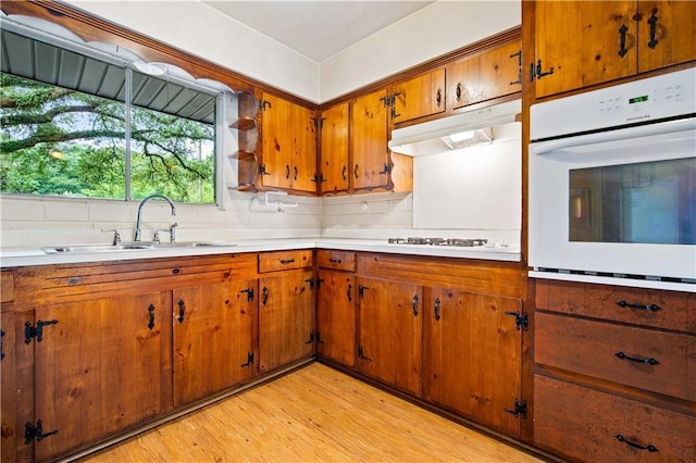 4359 Montclair Cir E, Mobile, AL 36693 - kitchen featuring white appliances, a sink, under cabinet range hood, brown cabinetry, and light wood-style floors