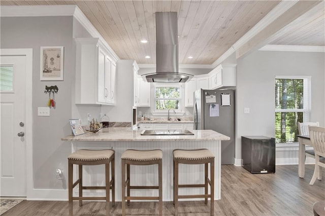 kitchen with ornamental molding, island range hood, black electric cooktop, white cabinets, and stainless steel refrigerator