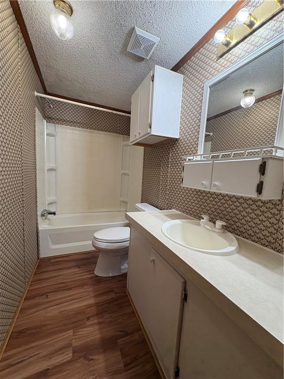 full bathroom featuring hardwood / wood-style floors, shower / bathing tub combination, vanity, toilet, and a textured ceiling