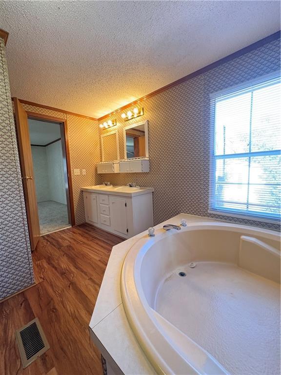 bathroom featuring wood-type flooring, a tub to relax in, ornamental molding, vanity, and a textured ceiling