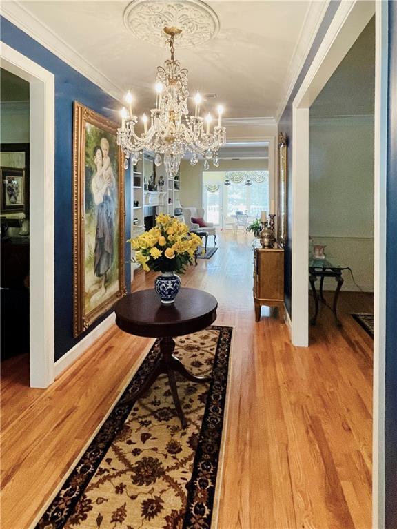 hall with hardwood / wood-style flooring, crown molding, and an inviting chandelier