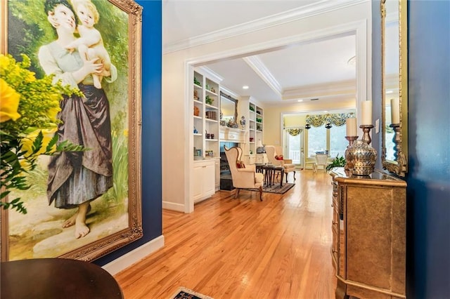 corridor featuring light hardwood / wood-style floors, built in features, crown molding, and a tray ceiling