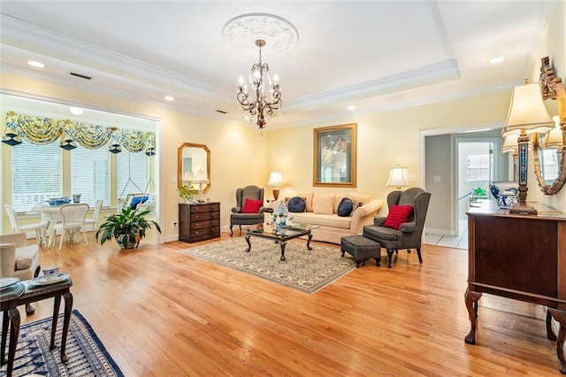 living room featuring an inviting chandelier, light wood-type flooring, crown molding, and a tray ceiling