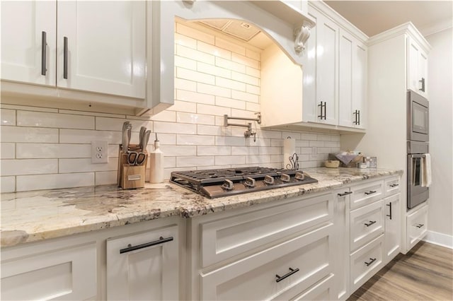 kitchen with white cabinetry, decorative backsplash, appliances with stainless steel finishes, light wood-type flooring, and light stone countertops