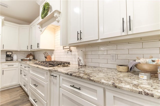 kitchen featuring white cabinetry, stainless steel gas cooktop, light stone counters, backsplash, and light hardwood / wood-style floors