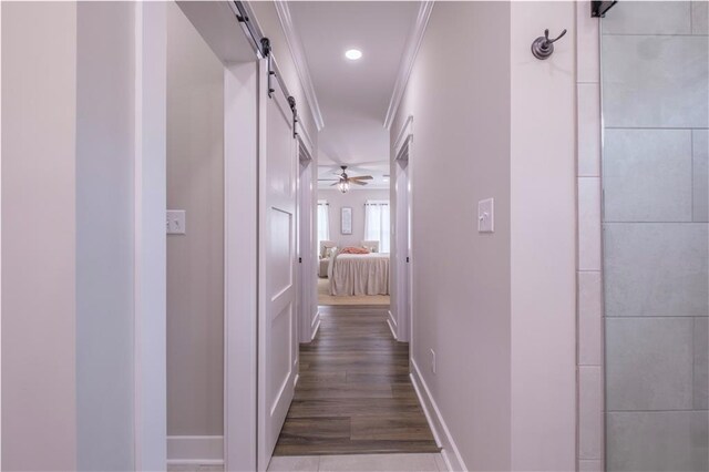 hall featuring a barn door, crown molding, and dark wood-type flooring