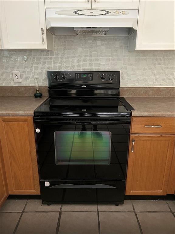 9016 Julie St, Mobile, AL 36608 - kitchen with electric range, under cabinet range hood, light tile patterned flooring, white cabinets, and backsplash