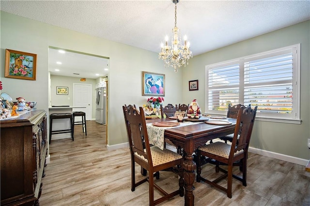 dining room with light hardwood / wood-style floors, a textured ceiling, and an inviting chandelier