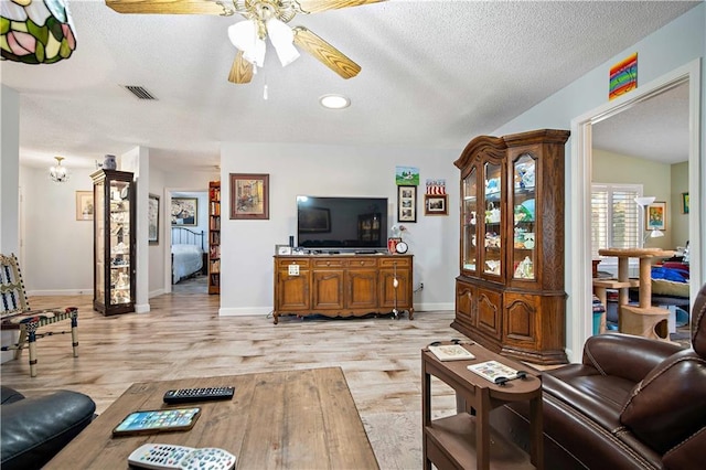 living room with a textured ceiling, light wood-type flooring, vaulted ceiling, and ceiling fan