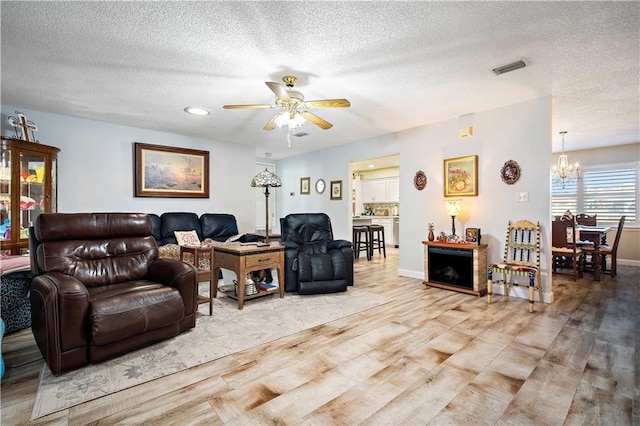 living room featuring ceiling fan with notable chandelier, a textured ceiling, and light wood-type flooring