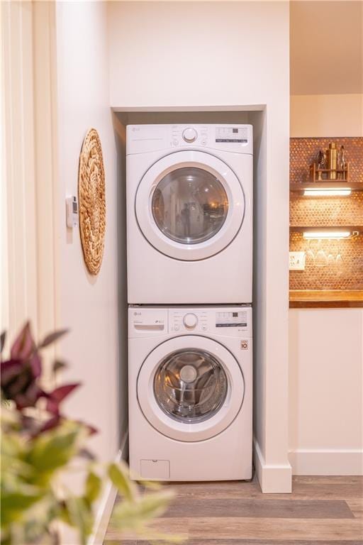 washroom featuring stacked washing maching and dryer, laundry area, baseboards, and wood finished floors