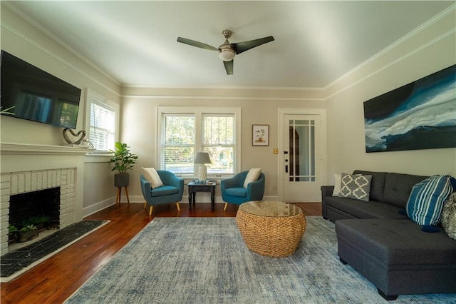 living area featuring baseboards, ceiling fan, dark wood-type flooring, crown molding, and a brick fireplace