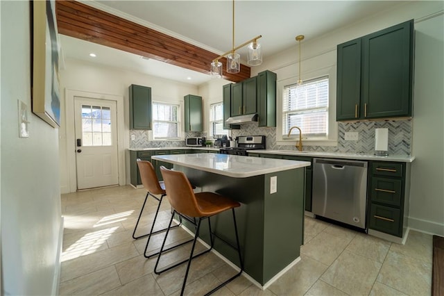 kitchen with appliances with stainless steel finishes, under cabinet range hood, a breakfast bar area, backsplash, and green cabinetry