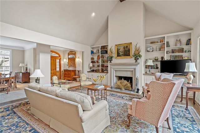 living area with built in features, a fireplace with raised hearth, ornamental molding, high vaulted ceiling, and light wood-type flooring