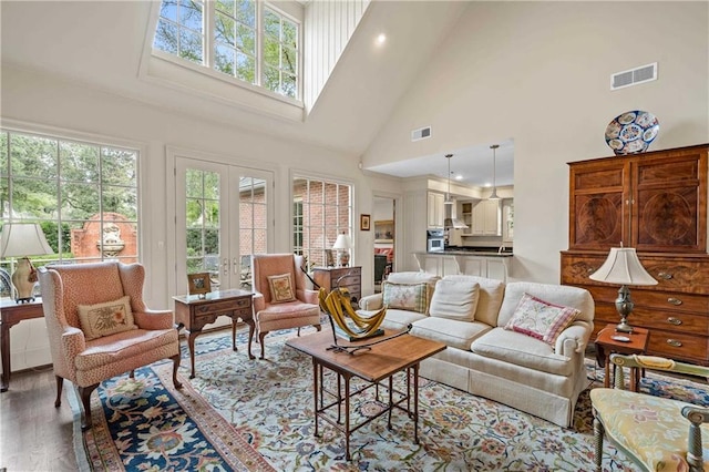 living room with french doors, visible vents, a towering ceiling, and wood finished floors